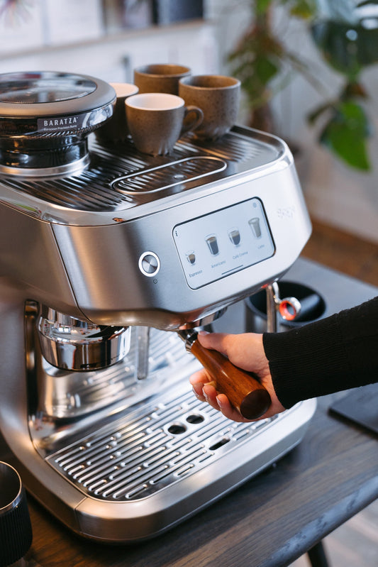 Hand haalt een portafilter met houten greep uit een Sage-espressomachine.