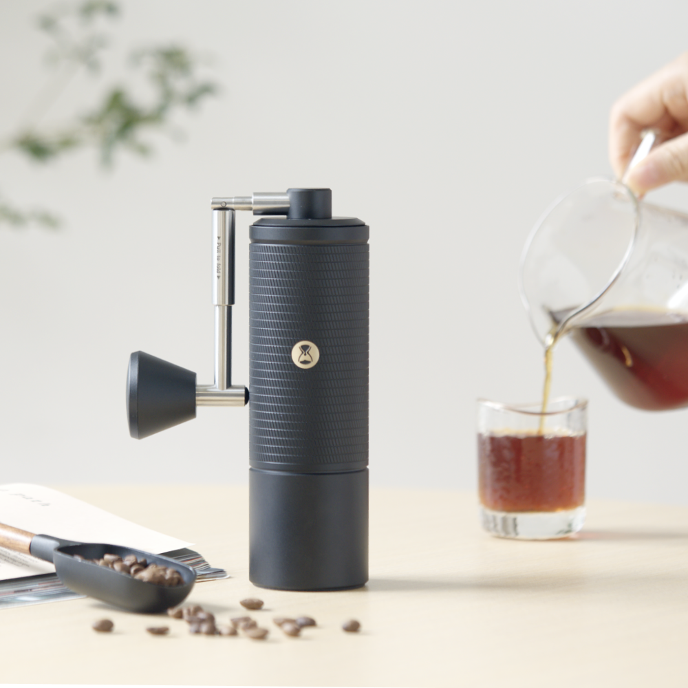 TIMEMORE Chestnut C5 Pro in zwart op tafel, naast een V60-kan die koffie in een glas schenkt